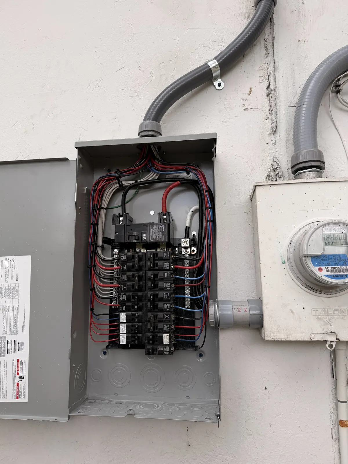 New breaker panel with neatly dressed wiring beside the meter, installed by Manny Source Electric